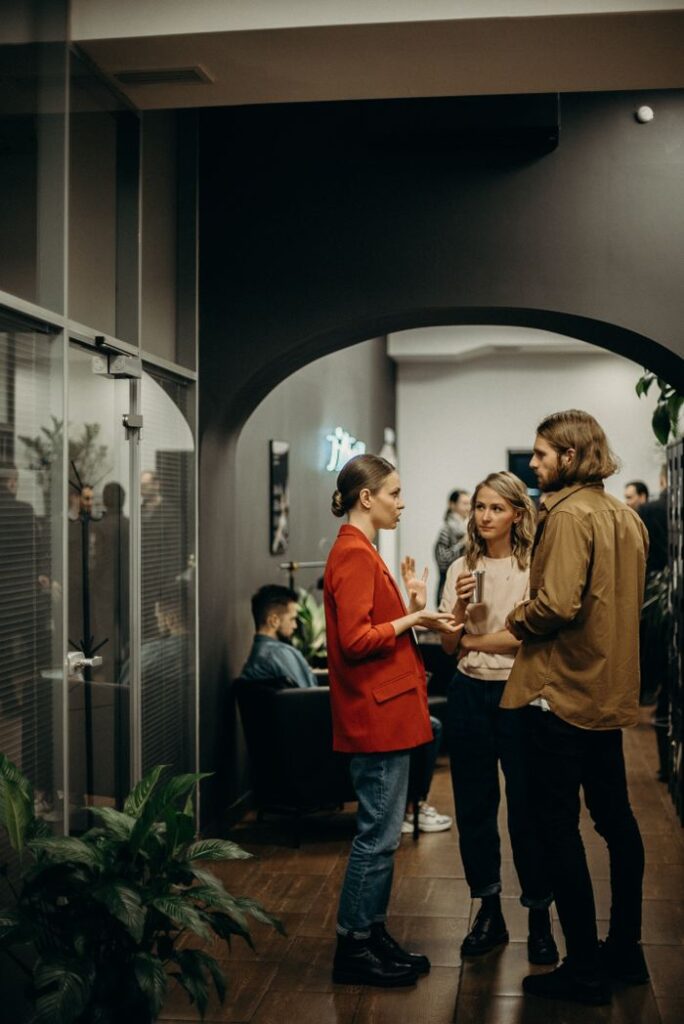 A lively casual office gathering with people engaged in conversation in a modern indoor setting.