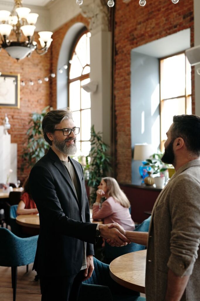 Two men shaking hands in a stylish cafe, surrounded by a warm ambiance and natural light.